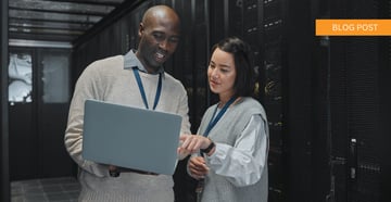 Information technology team of two standing in server room viewing open laptop together