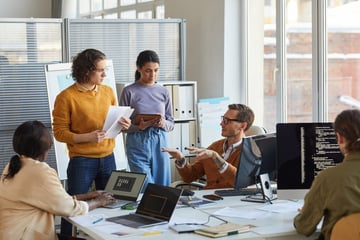 An IT development team meeting in an office with large windows.