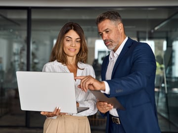 Two business people review information on a laptop in an office. 