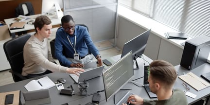 Employees reviewing CMMC 2.0 guidelines together on a computer in an office. 