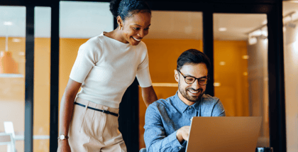 Two colleagues review organizational goals together using a laptop in a modern office.