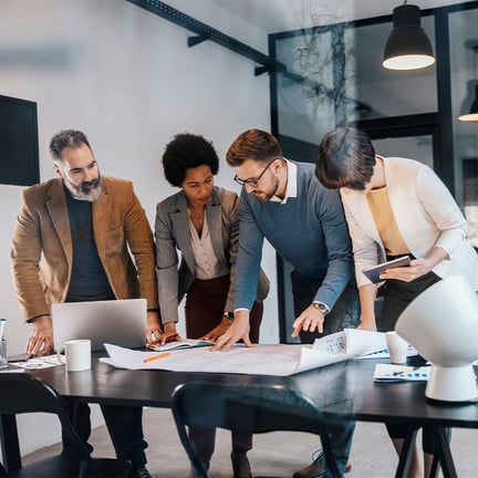 group of architects working together in an office looking at blueprints spread out on a desk