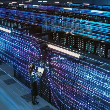 software developer standing in front of numerous servers holding laptop