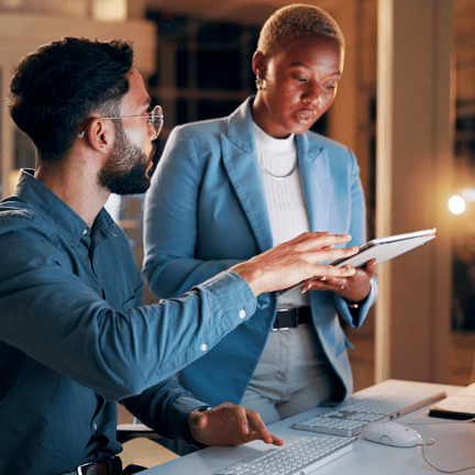 two colleagues collaborating over office desk using tablet device during evening