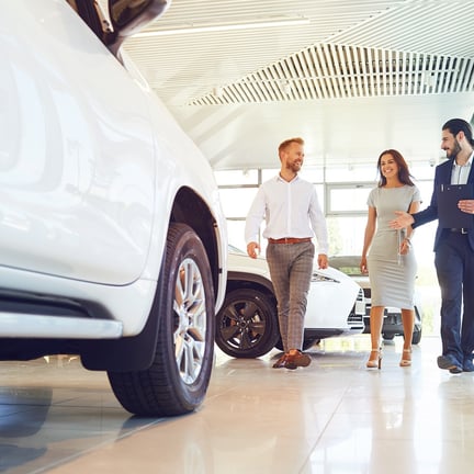 Couple and auto dealer selling cars look at car in showroom of dealership
