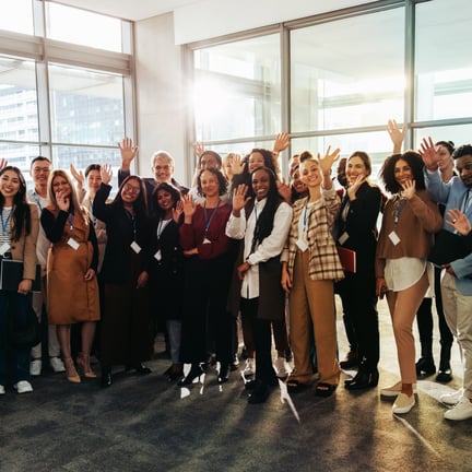 Diverse group happily waving inside modern conference room with large windows and bright natural light