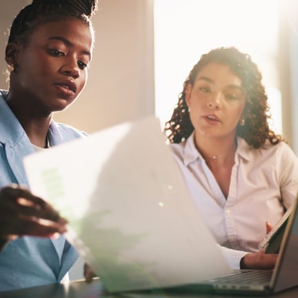 two business professionals discussing strategy over documents with laptop