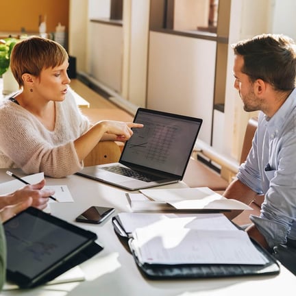 female executive showing data to team pointing to laptop screen