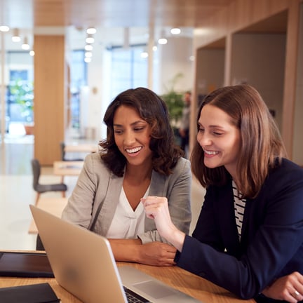 pair of smiling IT consultants working together on laptop in a modern office