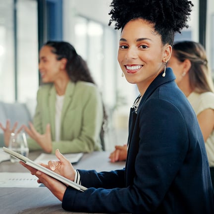smiling young professional looking at camera in business meeting holding tablet device