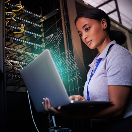 female IT professional monitoring secure cloud services on laptop amongst servers