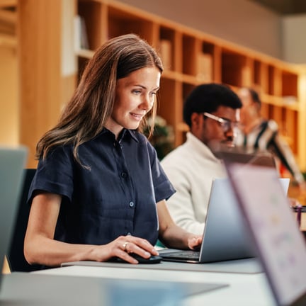 young professional seated at desk in library in front of laptop working on project planning