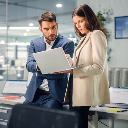 two colleagues leaning against office desk discussing strategy over laptop