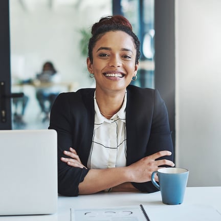smiling young businesswoman arms crossed casually working at her desk in a modern office