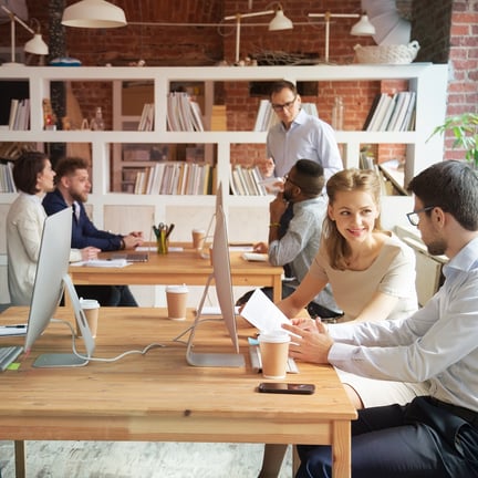 diverse group of professionals seated amongst desktop computers in well-lit office discussing business strategy