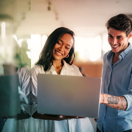 colleagues standing together and reviewing information on a portable laptop smiling